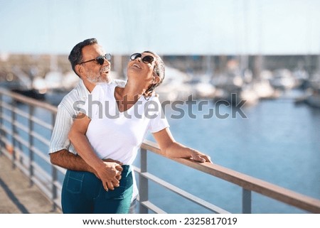 Summer Love Story. Romantic Senior Couple Embracing Expressing Happiness Standing At Marina Pier Outside, Smiling And Laughing In Joy On Summer Day At Seaside. Sea Holidays In Older Age. Free Space