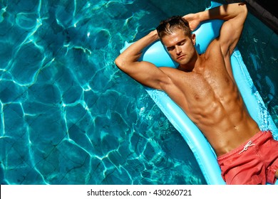 Summer Man Body Sun Skin Care. Beautiful Model With Sexy Body In Swimwear Tanning, Floating On Mattress In Swimming Pool Water. Fitness Male With Healthy Tan Relaxing At Relax Spa Resort. Summertime