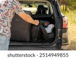 In the summer, a man is going to go on vacation by car. He loads luggage into the trunk of his car (from the series "Luggage").