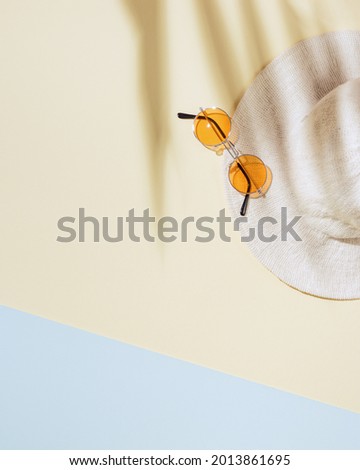 Summer minimal background with wide-brimmed hat, colored sunglasses on sandy color background with sun shadows and copy space. Summertime concept pastel colored aesthetic photo.