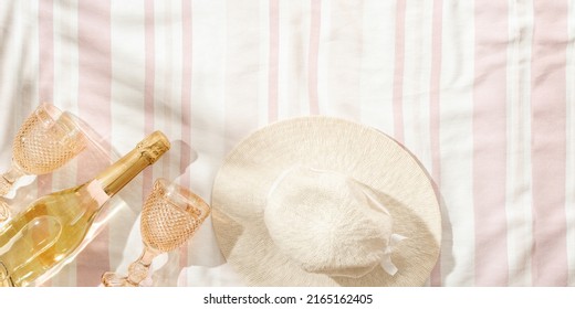 Summer Minimal Flatlay With Wide-brimmed Hat, Colored Wine Glasses, Champagne Wine, Sparkling White Wine On Striped Beach Towel As Background, Sun Shadows. Summer Pastel Colored Aesthetic Banner.