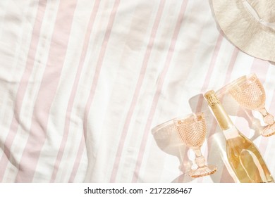 Summer Minimal Flatlay With Wide-brimmed Hat, Colored Wine Glasses, Champagne Wine, Sparkling White Wine On Striped Beach Towel As Background, Sun Shadows. Summer Pastel Colored Aesthetic Photo.