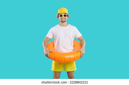 Summer mood. Portrait of cheerful young man with inflatable circle for swimming on light blue background. Caucasian guy in shorts, T-shirt, panama, sunglasses and with inflatable circle at the waist. - Shutterstock ID 2228842221