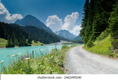 summer mountain landscape with turquoise lake and gravel road bordered by wildflowers in the Swiss Alps near Arosa
