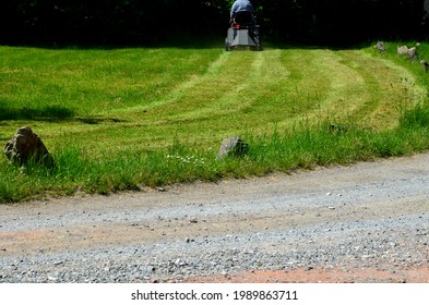 Summer Mowing Of Grass. Man On A Tractor Mows The Rows Of Lawn By The Path In The Park. Demanding Work With Lots Of Exhaust Noise And Vibrations