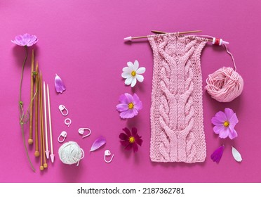 Summer Needlework. Knitted Headband With Voluminous Braids Of Pink Threads. Fresh Cosmea Flowers And A Set Of Knitting Needles On A Pink Background. Top View, Closeup, Flat Lay, Copy Space, Mockup