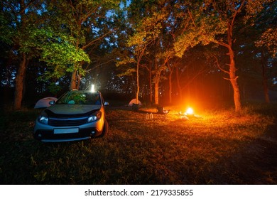 Summer Night Capmpfire In Forest Near Silver Car And Two Tents And Portable Chairs