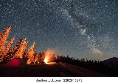 Summer night in mountains. Starry sky over camping on hills. Warm light from campfire at dark night. - Shutterstock ID 2282846273