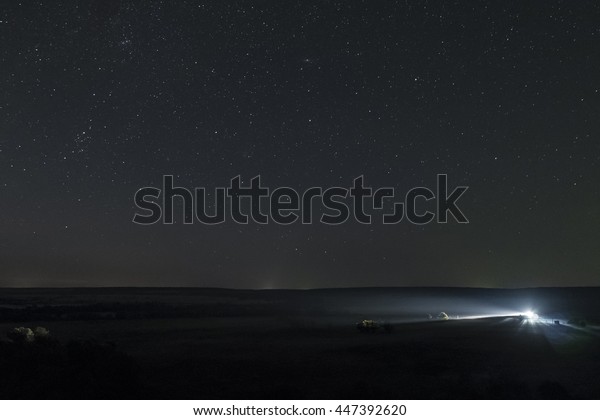 Summer night sky high above\
the plain. Single distant car lights at night meadow with clear\
starry sky.