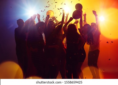 Summer nights. A crowd of people in silhouette raises their hands on dancefloor on neon light background. Night life, club, music, dance, motion, youth. Yellow-blue colors and moving girls and boys. - Shutterstock ID 1558659425