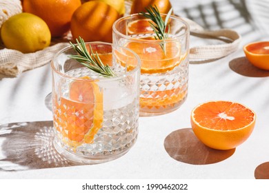 Summer orange cocktails with citrus fruits on white background. Hard seltzer, lemonade, refreshing drinks, low alcohol mocktails, summer party concept. Trendy palm leaf shadow and sunlight, sun