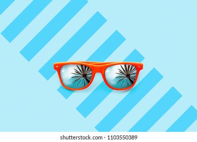 Summer Orange Sunglasses With Palm Trees Reflections Isolated In Large Blue Background With Partial Stripes. Minimal Concept: Summer Holidays, Sun Protection, Hot Days And Tropical Travel Vacations