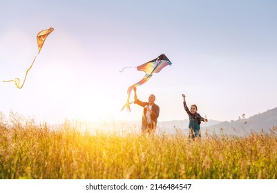 Summer outdoor photo of smiling father with daughter as they releasing colorful kites on the high grass meadow. Warm family moments or outdoor time spending concept image. 