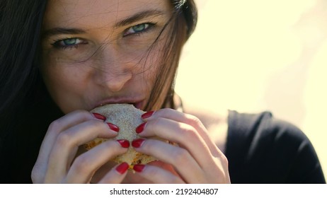 Summer, Outdoors. Portrait Of Beautiful Brunette Woman, With Dark Hair, With Apetite Eating Fastfood, Sexually Biting Hamburger. She Has Chubby Lips. High Quality Photo