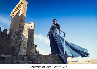 Summer outdoors portrait of beautiful furious scandinavian warrior ginger woman in grey dress with metal chain mail. Fortress Sudak, Crimea