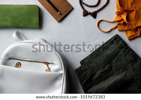 Women’s summer outfit: green sneakers, yellow top, army green shorts, white backpack, green wallet. Fresh-coloured flat layout representing modern youth lifestyle.