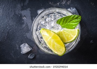 Summer paloma cocktail, vodka lime, mojito or gin tonic with lime wedge and crushed ice in rocks, two cold alcohol beverage glasses on black background copy space