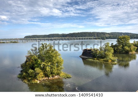 
Summer panorama of the Susquehanna River from old, Civil War bridge foundation remnants in Wrightsville, PA. Cloudy blue sky reflected in the water. Wrights Ferry Bridge, US Route 30 on the horizon.