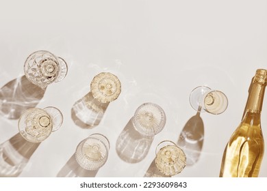 Summer party drinks flat lay, wine glasses with white sparkling wine and sunshine shadow on light table. Minimal pattern with beautiful wine glasses, above view still life, beige golden neutral color