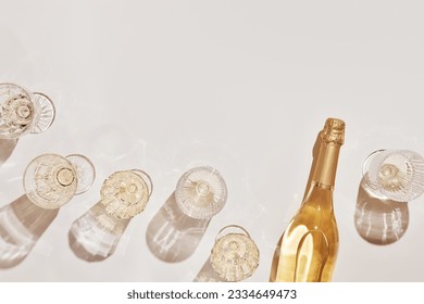 Summer party drinks flat lay, wine glasses with white sparkling wine and sunshine shadow on light table. Minimal pattern with beautiful wine glasses, above view still life, beige golden neutral color
