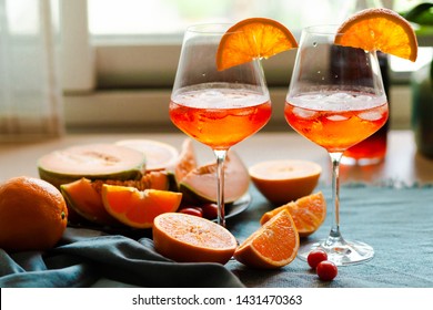 Summer Party: Two Cocktails  Aperol Spritz Are Served With Ice In Wine Glasses, Decorated With Orange Slices. Blue Contrast Background, Extremely Bright Colors. Fresh Fruits Is Accompaniment. 