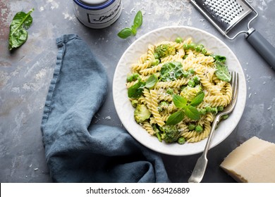 Summer Pasta With Green Peas, Broccoli, Spinach, Basil, Creamy Pesto Sauce And Parmesan Cheese On Concrete Background; Overhead Shot