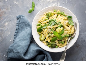 Summer Pasta With Green Peas, Broccoli, Spinach, Basil, Creamy Pesto Sauce And Parmesan Cheese On Concrete Background; Overhead Shot; Copy Space