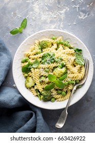 Summer Pasta With Green Peas, Broccoli, Spinach, Basil, Creamy Pesto Sauce And Parmesan Cheese On Concrete Background; Overhead Shot