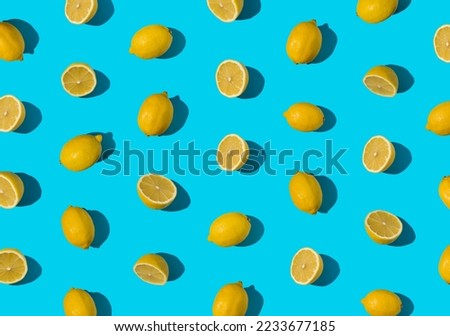 Summer pattern made with fresh cut and whole yellow lemon on bright light blue background. Minimal background summer concept on with harsh light and sharp shadow