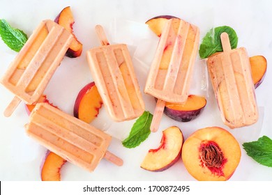 Summer peach yogurt ice pops, top view scattered on a white marble background