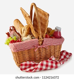 Summer picnic basket filled with food with fresh fruit and juice, spicy salami, baguettes, tomatoes and herb spread isolated on white on a rustic checked tablecloth