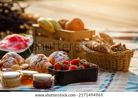 summer picnic basket with fruit and bakery on a blanket outdoors. Lunch with croissants, jam, watermelon, strawberry and fresh fruits in wooden box in the park. Copy space