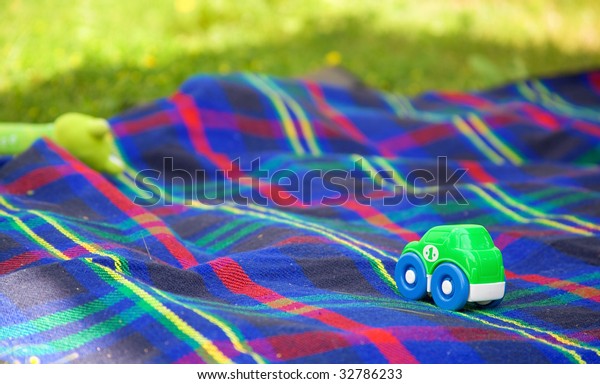 Summer picnic with a child.\
Small toy car on a checkered blanket laid on the grass for children\
games