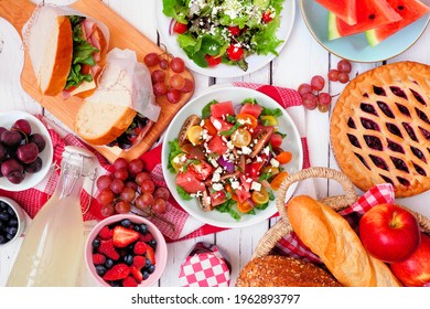 Summer Picnic Food Table Scene With Cold Salads, Sandwiches, Fruit And Treats. Overhead View On A White Wood Background. Copy Space.