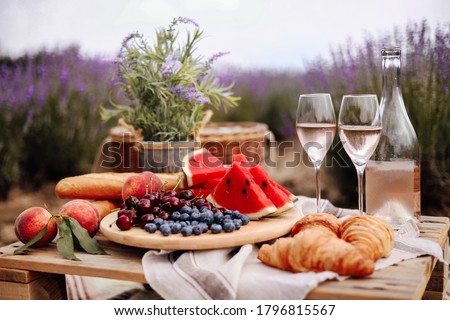 A summer picnic in a lavender field with watermelon, croissants and a bottle of rose wine and two glasses. Beautiful rustic decor. Gorizontal format.