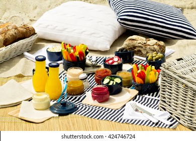 Summer picnic on the beach. Serving picnic utensils blue with vegetables and sauces on striped tablecloths and knitted pillow. Selective focus.