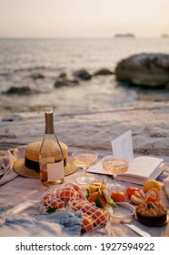 Summer picnic outdoors with blanket, eco style straw hat with fruits and wine. Romantic picnic with seaside and sea view at sunset