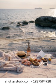Summer picnic outdoors with blanket, eco style straw hat with fruits and wine. Romantic picnic with seaside and sea view at sunset