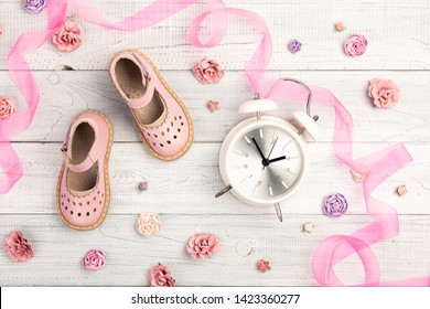 Summer Pink Baby Girl Shoes And Card It Is A Girl In An Envelope, And Roses, Ribbon, Alarm Clock On Wooden Background. Top View Trendy Leather Sandal, Flat Lay. Copy Space For Your Text