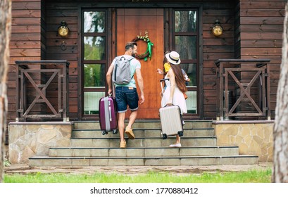 Summer Pleasure. A Photo From Behind Of A Glad Travelling Family With Suitcases And Backpacks Coming To The Hotel, Going Up Stairs, Father And Mother Looking At Each Other.