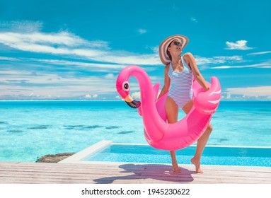 Summer pool fun swimsuit model posing in pink flamingo float showing off slim figure bikini ready body for luxury Caribbean vacation getaway. Woman having fun by hotel infinity pool.
