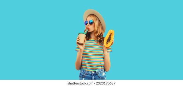 Summer portrait of beautiful young woman with juicy papaya fruit drinking fresh juice looking away wearing straw hat on blue background - Shutterstock ID 2323170637