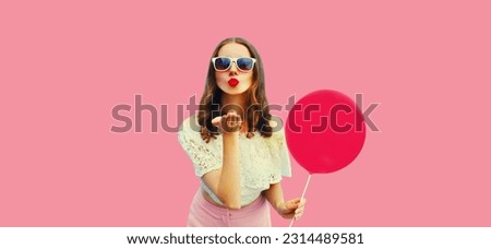 Summer portrait of beautiful young woman blowing her lips sending sweet air kiss with balloon on pink background