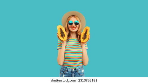 Summer portrait of happy cheerful young woman having fun with fresh papaya fruits wearing straw hat, sunglasses on blue background - Shutterstock ID 2310963181
