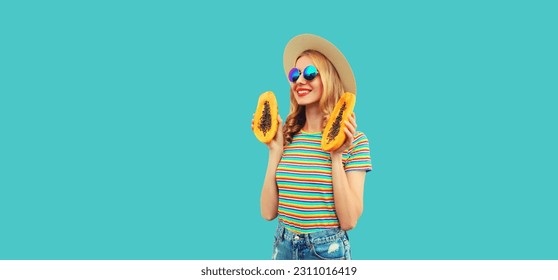 Summer portrait of happy cheerful young woman having fun with fresh papaya fruits wearing straw hat, sunglasses on blue background - Shutterstock ID 2311016419