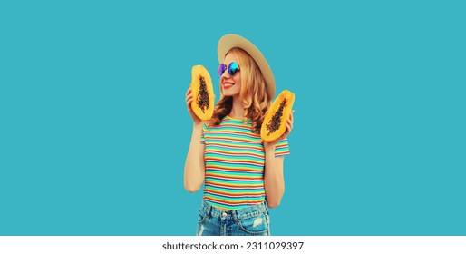 Summer portrait of happy cheerful young woman having fun with fresh papaya fruits wearing straw hat, sunglasses on blue background - Shutterstock ID 2311029397