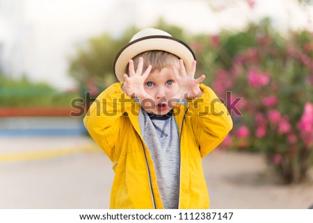 Summer portrait of happy child boy in straw hat, smile and laughs on camera and show something great or big with hands. Three years old kid with beautiful smile outdoors in park.