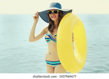 Summer portrait of happy smiling woman with inflatable circle wearing a straw hat on a beach, sea background