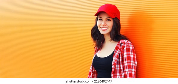 Summer portrait of happy smiling young woman wearing a red baseball cap on colorful orange background - Powered by Shutterstock