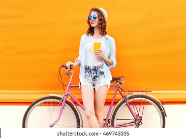 Summer portrait of happy smiling young woman with coffee or juice cup and retro vintage bicycle on colorful orange background - Powered by Shutterstock